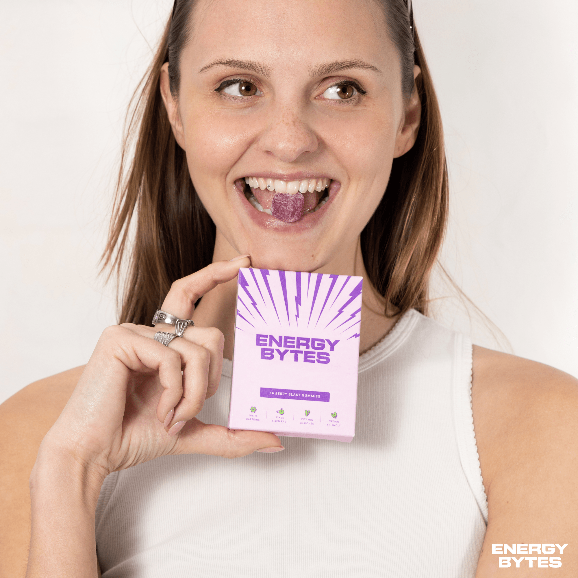 Cheerful woman with a radiant smile holding a pack of Energy Bytes Berry Blast Gummies, showcasing the natural, quick-energy snack with a visible Energy Bytes logo