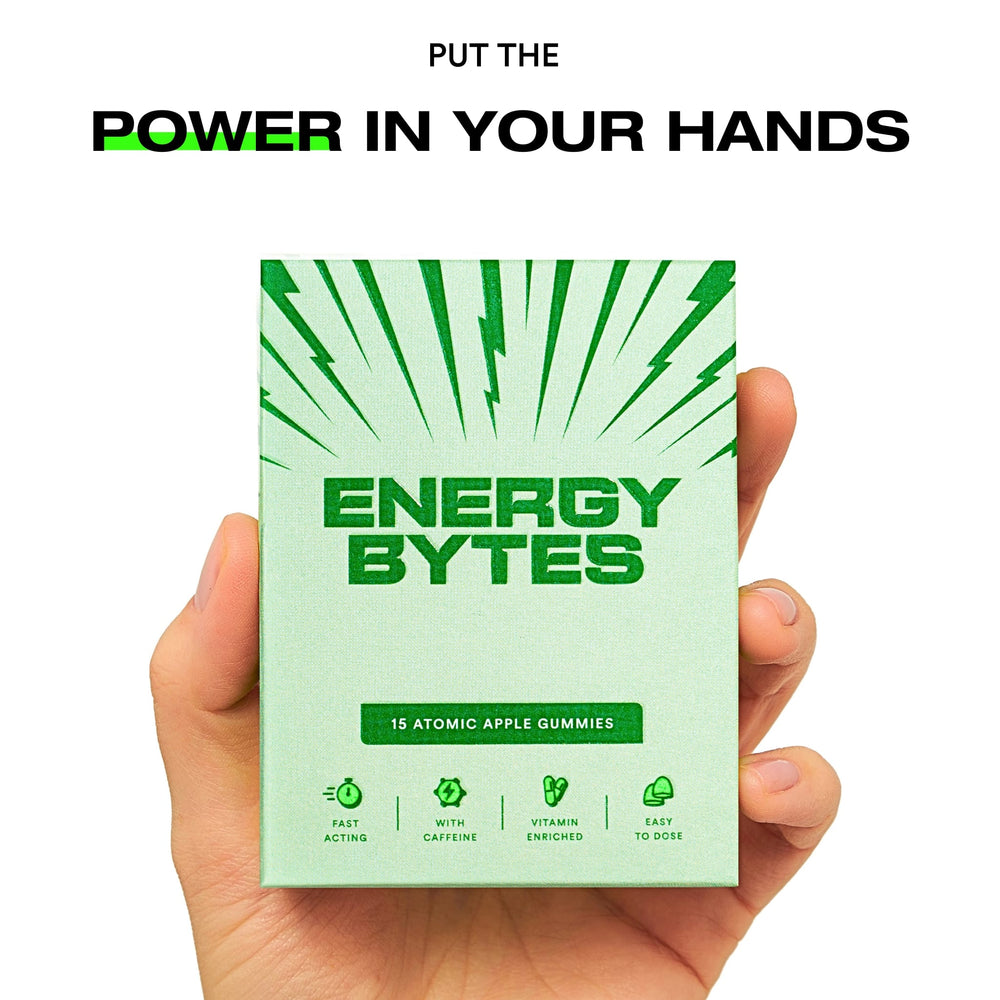 Hand holding a pack of Energy Bytes Atomic Apple Gummies with text above reading 'PUT THE POWER IN YOUR HANDS'.