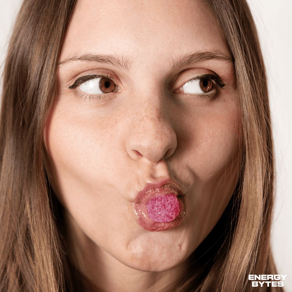 Woman puckering lips while sampling a Wild Strawberry Energy Bytes gummy, capturing the vibrant, on-the-go snacking experience.